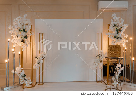 Elegant Wedding Backdrop with Floral Arrangements: Gold Frames, White Flowers, and Candlelight Ceremony Setting. Elegant Wedding Backdrop with Floral Arrangements: Gold Frames, White Flowers, and Candlelight Ceremony Setting. 127440796