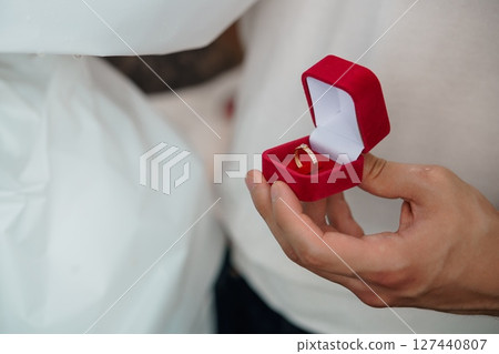 Wedding Rings Exchange Ceremony, Close-Up of Hands Holding Red Box, Symbolic Love Commitment, Golden Bands, Elegant Style. Wedding Rings Exchange Ceremony, Close-Up of Hands Holding Red Box, Symbolic Love Commitment, Golden Bands, Elegant Style. 127440807