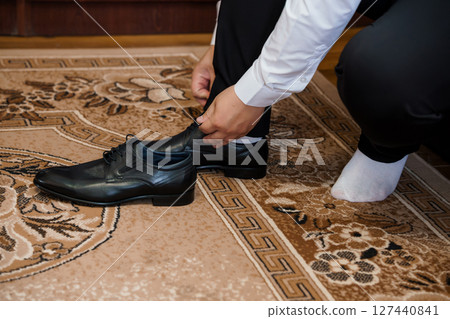 Groom Getting Ready: Man Tying Black Dress Shoes Before Wedding, Sophisticated Style, Carpet, Formal Attire, Black and White Palette. Groom Getting Ready: Man Tying Black Dress Shoes Before Wedding, Sophisticated Style, Carpet, Formal Attire, Black and White Palette. 127440841
