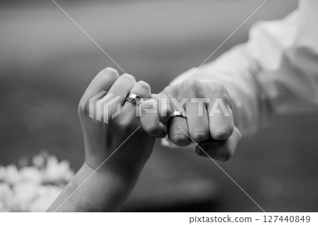 Couple Holding Hands with Wedding Rings, Black and White Love Scenario, Close-Up View of Intertwined Fingers, Symbolism of Commitment and Union. 127440849