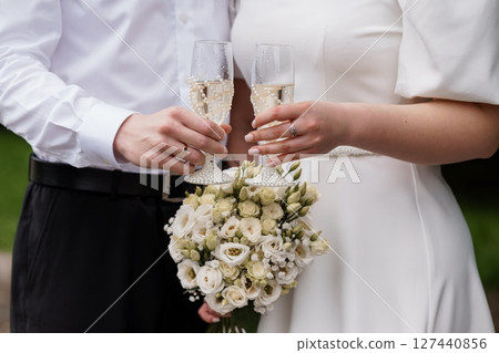Romantic Wedding Celebration with Champagne Toast. Elegant Couple, White Bouquet, Close-Up Shot, Rings, Ivory and Pearl Tones, Fine Art Style. Romantic Wedding Celebration with Champagne Toast. Elegant Couple, White Bouquet, Close-Up Shot, Rings, Ivory and Pearl Tones, Fine Art Style. 127440856