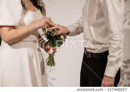 Wedding Ceremony Exchange of Rings: Close-Up of Hands Holding Bouquet. White Dress, Black Suit. Emotional Commitment, Symbolic Gesture. 127440857