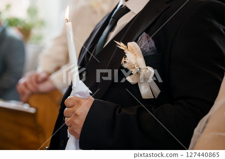 Orthodox Wedding Candle Lighting Ceremony: Groom Holding Candle, Black Suit Boutonniere, Church Interior, Rustic Bohemian Florals, Golden Light. Orthodox Wedding Candle Lighting Ceremony: Groom Holding Candle, Black Suit Boutonniere, Church Interior, Rustic Bohemian Florals, Golden Light. 127440865
