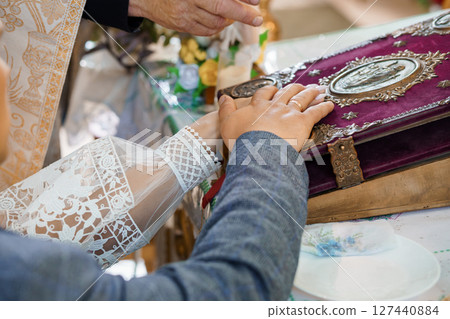 Hands Joined Over Religious Book During Wedding Ceremony: Lace Cuffs, Purple Velvet Cover, Golden Details, Intimate Celebration. 127440884