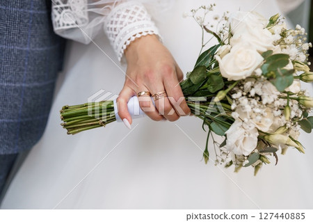 Wedding Rings and White Bouquet. Close-up of Hands Holding Flowers. Elegant Rose and Baby's Breath. Gold Bands. Marriage Symbolism. 127440885