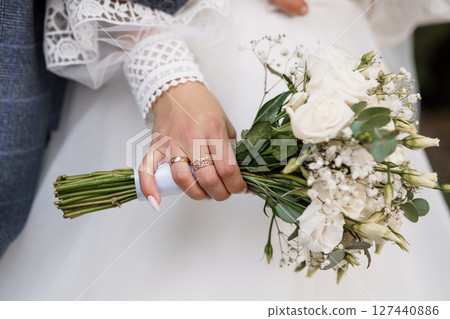 Close-up of Brides Hands Holding Bouquet and Wedding Rings, Romantic White Flowers, Lace Dress, Gold Jewelry, Celebration, Love, Elegant Style 127440886
