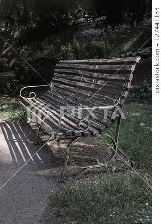 One empty bench made of old wooden boards and black iron stands in the park. One empty bench made of old wooden boards and black iron stands in the park. 127441133