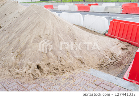 Red and white plastic barriers blocking the road. Pile of sand. Road repairs in the city 127441332