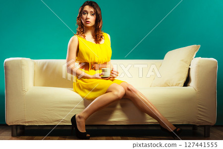 woman sitting on sofa holds coffee cup 127441555