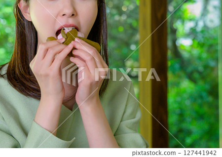 A summer afternoon moment as a woman enjoys Japanese sweets with a gentle expression on her face, holding them in both hands. A summer afternoon moment as a woman enjoys Japanese sweets with a gentle expression on her face, holding them in both hands. 127441942