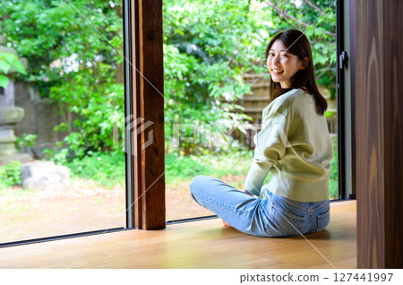 A summer Japanese-style portrait of a woman sitting on a veranda, turning around and smiling from behind with a green background A summer Japanese-style portrait of a woman sitting on a veranda, turning around and smiling from behind with a green background 127441997