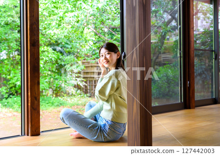 A peaceful and natural portrait of a woman sitting on a veranda in summer, smiling and looking at the camera A peaceful and natural portrait of a woman sitting on a veranda in summer, smiling and looking at the camera 127442003