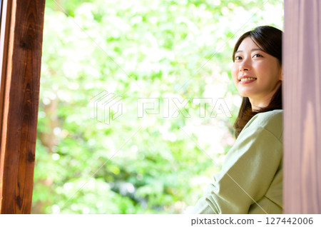 A relaxing summer scene with a woman smiling and looking at the view outside while surrounded by natural light 127442006