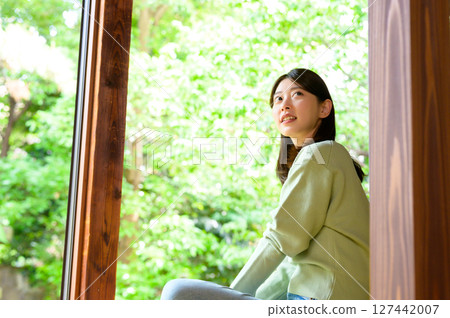 A quiet summer moment as a woman sits on the veranda and gazes at the greenery with a calm expression 127442007