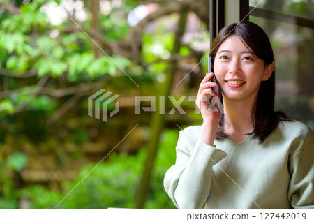 A natural summer portrait of a woman smiling while talking on her smartphone against a green background A natural summer portrait of a woman smiling while talking on her smartphone against a green background 127442019
