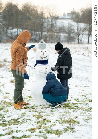 Family building a snowman together in a snowy field. Winter fun and family bonding. Family building a snowman together in a snowy field. Winter fun and family bonding. 127442185