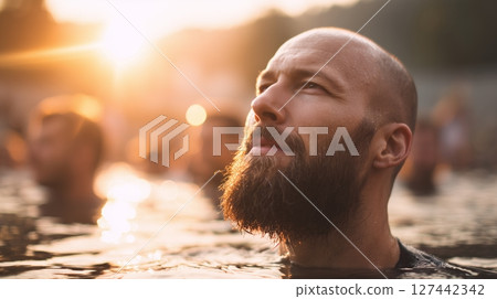Man with beard immersed in water during baptismal ritual at sunset, surrounded by people expressing faith and spirituality in nature Man with beard immersed in water during baptismal ritual at sunset, surrounded by people expressing faith and spirituality in nature 127442342