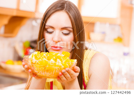 Woman holds bowl full of sliced orange fruits 127442496