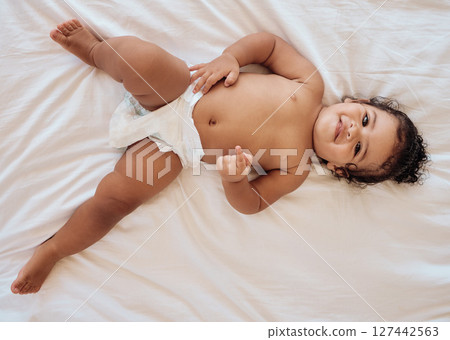 Happy baby, smile and relax on bed in family home bedroom for diaper change, bedtime or healthy childcare. Child, happiness and body care in disposable nappy or kids portrait from above in nursery 127442563