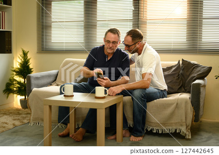 Senior man and adult son enjoying a warm conversation while using a mobile phone together. Father day concept Senior man and adult son enjoying a warm conversation while using a mobile phone together. Father day concept 127442645