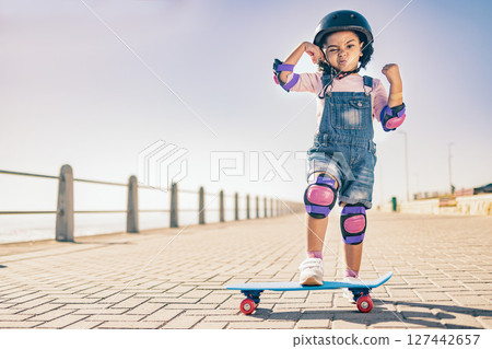 Children, skate and strong with a girl on her skateboard for fun on the beach promenade alone during summer. Muscle, bicep and helmet with a female child skating outside on a sidewalk with knee pads Children, skate and strong with a girl on her skateboard for fun on the beach promenade alone during summer. Muscle, bicep and helmet with a female child skating outside on a sidewalk with knee pads 127442657