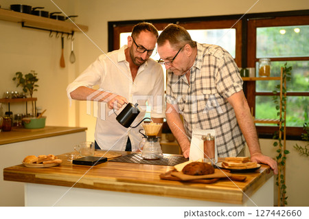 Senior man and son making pour over coffee in a cozy kitchen. Father day concept Senior man and son making pour over coffee in a cozy kitchen. Father day concept 127442660