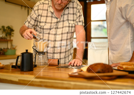 Senior man and son making pour over coffee in a cozy kitchen. Father day concept Senior man and son making pour over coffee in a cozy kitchen. Father day concept 127442674