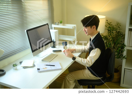 Young man shopping online with a credit card in hand, seated at a modern home office desk 127442693