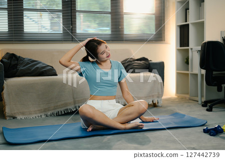 Young woman wearing sportswear practices stretching exercises in her living room 127442739