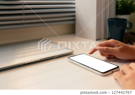 Close up of hands using a smartphone with a blank screen on a white desk 127442767