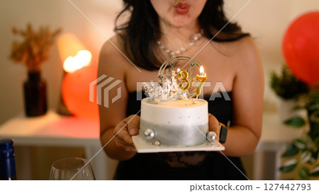 Glamorous birthday celebration with a fashionable woman blowing out candles on a 37th birthday cake 127442793