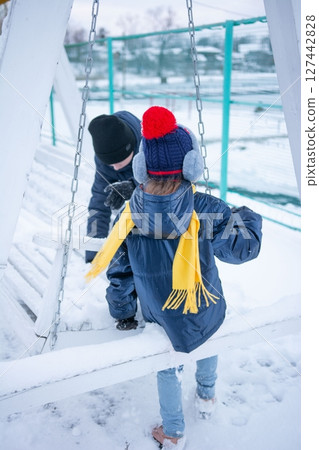 Children playing in the snow on a swing set. Winter fun and outdoor activities. 127442828