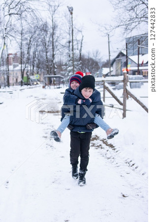 A playful piggyback ride in the snow. Two children enjoy a winter adventure, laughter echoing through the frosty air. A playful piggyback ride in the snow. Two children enjoy a winter adventure, laughter echoing through the frosty air. 127442833