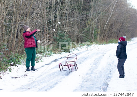 A playful snowball fight unfolds in a snowy forest. An adult and child engage in winter fun near a small sled. 127442847