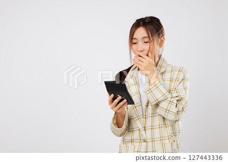 Asian woman with calculator looks shocked, staring at the calculator display, surprised by unexpected tax numbers in her financial accounting report. isolated studio white background, Tax day concept Asian woman with calculator looks shocked, staring at the calculator display, surprised by unexpected tax numbers in her financial accounting report. isolated studio white background, Tax day concept 127443336