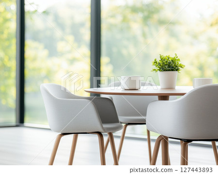 Modern dining area with stylish chairs and potted plant, featuring large windows that bring in natural light and serene atmosphere 127443893