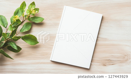 blank white book cover on cozy wooden table with green leaves nearby blank white book cover on cozy wooden table with green leaves nearby 127443929