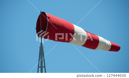Windsock indicator of wind. Wind cone indicating wind direction and force. Horizontally flying windsock with blue sky in the background 127444030
