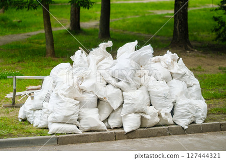 Waste material stacked in white bags in a park area during daytime Waste material stacked in white bags in a park area during daytime 127444321