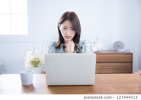 Cute woman thinking and worrying while looking at a computer in a room, a little serious, negative image, surprised and shocked 127444513