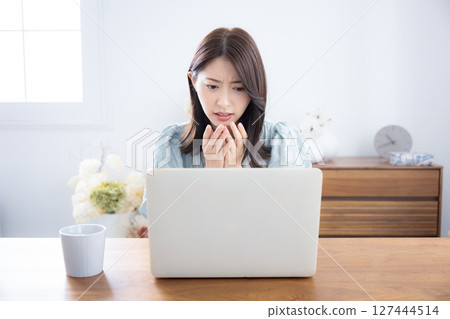 Cute woman thinking and worrying while looking at a computer in a room, a little serious, negative image, surprised and shocked 127444514