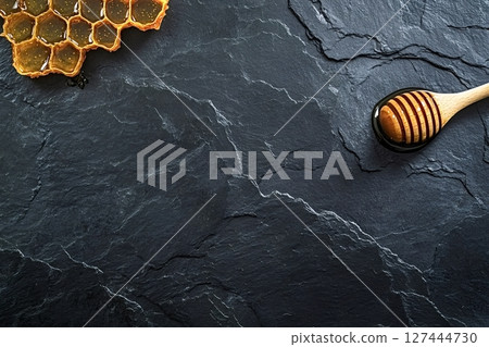 Honeycomb and honey dipper resting on dark stone surface 127444730