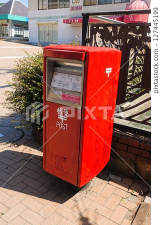 A vermilion mailbox on a street corner 127445199