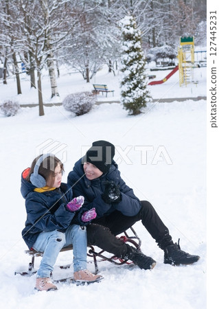 Siblings enjoy a snowy day sledding together in a park, laughing and playing in the winter wonderland. Siblings enjoy a snowy day sledding together in a park, laughing and playing in the winter wonderland. 127445231