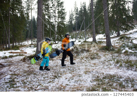 Excitement fills the air as two snowboarders walk through a snowy forest in winter, ready to embrace the thrill of gliding down the slopes ahead Excitement fills the air as two snowboarders walk through a snowy forest in winter, ready to embrace the thrill of gliding down the slopes ahead 127445403