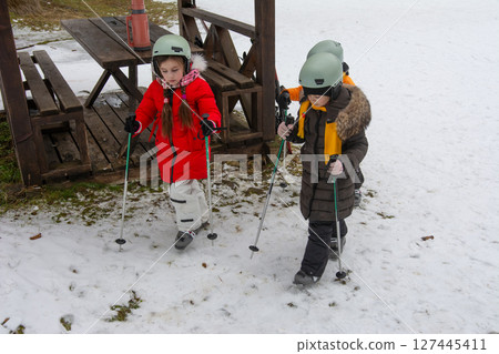 Winter fun unfolds as children navigate snowy terrain with skis and poles, cherishing the joy of outdoor adventure in a picturesque snowy landscape Winter fun unfolds as children navigate snowy terrain with skis and poles, cherishing the joy of outdoor adventure in a picturesque snowy landscape 127445411