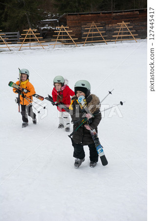 Excited children exploring a snowy landscape while preparing for their first skiing adventure with vibrant outfits and enthusiastic smiles in a winter wonderland Excited children exploring a snowy landscape while preparing for their first skiing adventure with vibrant outfits and enthusiastic smiles in a winter wonderland 127445417