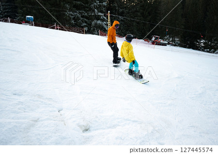 Two enthusiastic snowboarders glide down a snowy slope under a clear winter sky in a picturesque mountain resort during the afternoon Two enthusiastic snowboarders glide down a snowy slope under a clear winter sky in a picturesque mountain resort during the afternoon 127445574
