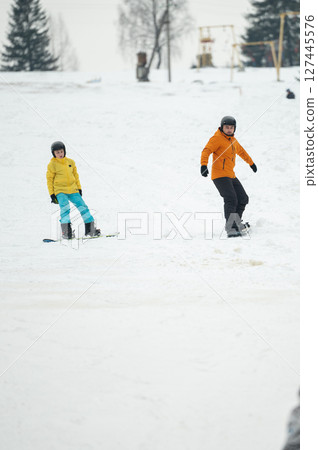 Snowy day filled with joy as two children enjoy snowboarding together on a white snowy hill surrounded by winter trees in the cool atmosphere of the season 127445576