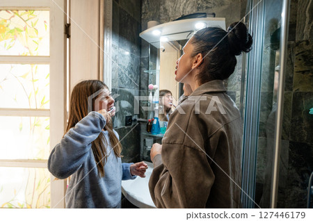 Sisters share a joyful moment while brushing teeth in a cozy bathroom filled with natural light and playful reflections of childhood memories 127446179